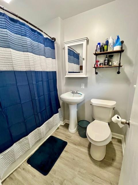 full bath with toilet, a shower with shower curtain, baseboards, and wood finished floors