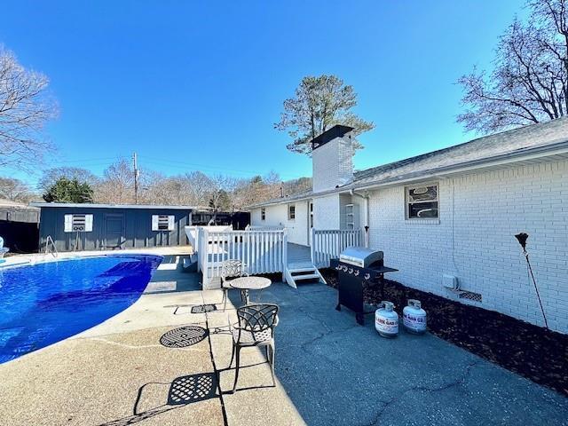 exterior space featuring a deck, a chimney, a patio, brick siding, and a fenced in pool