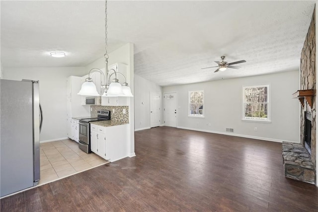 kitchen featuring a fireplace, stainless steel appliances, backsplash, wood finished floors, and ceiling fan with notable chandelier