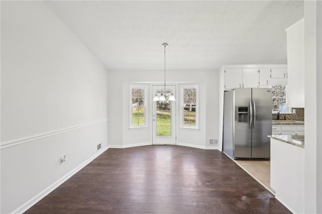 unfurnished dining area with a sink, a notable chandelier, baseboards, and wood finished floors