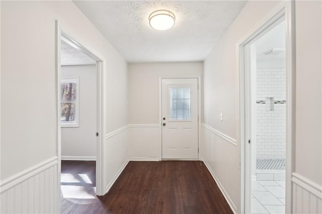 doorway with a textured ceiling, a wainscoted wall, and wood finished floors