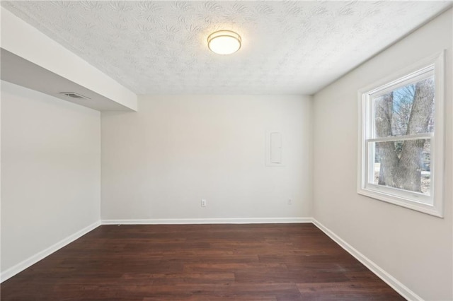 unfurnished room featuring dark wood-style floors, visible vents, a textured ceiling, and baseboards