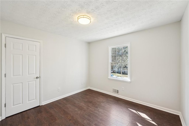 empty room with baseboards, visible vents, dark wood finished floors, and a textured ceiling