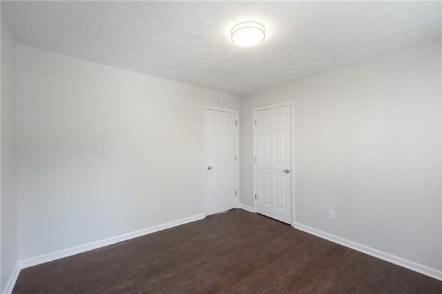 spare room with baseboards, dark wood finished floors, and a textured ceiling