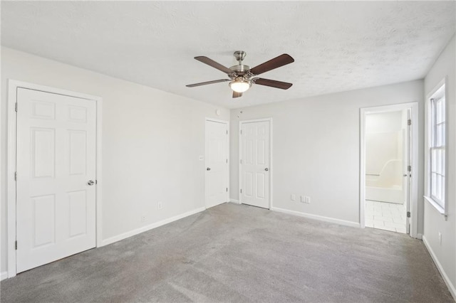 unfurnished bedroom featuring carpet, a ceiling fan, connected bathroom, a textured ceiling, and baseboards