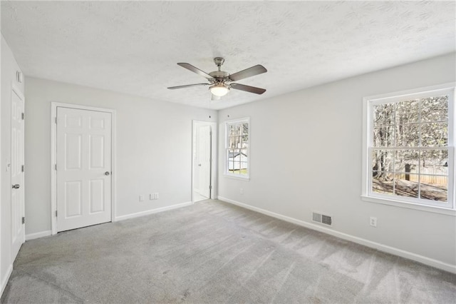 carpeted spare room with baseboards, visible vents, ceiling fan, and a textured ceiling