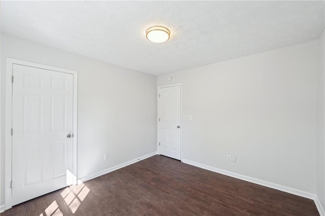 empty room featuring a textured ceiling, dark wood-type flooring, and baseboards