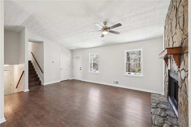 unfurnished living room with baseboards, a ceiling fan, dark wood-style flooring, a textured ceiling, and a stone fireplace