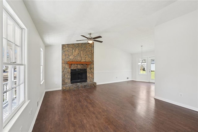 unfurnished living room with lofted ceiling, a stone fireplace, ceiling fan with notable chandelier, and dark wood finished floors