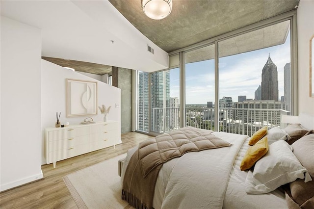bedroom with light wood finished floors, expansive windows, a city view, and access to exterior