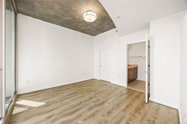 unfurnished bedroom with wood finished floors, ensuite bath, and baseboards