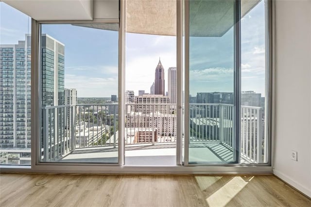 doorway to outside with plenty of natural light, wood finished floors, a skyline view, floor to ceiling windows, and baseboards