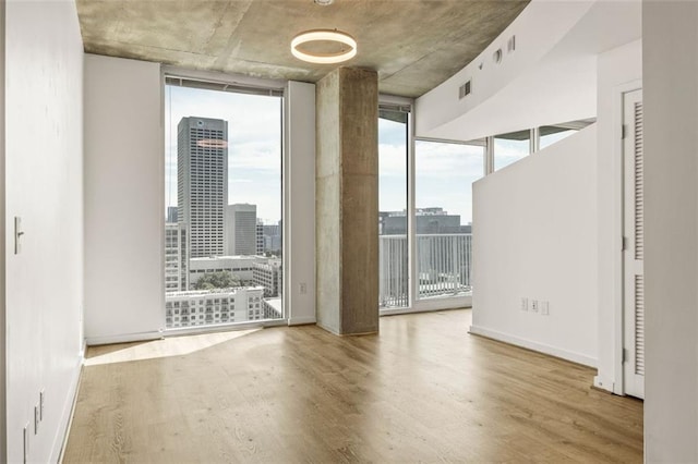 unfurnished room featuring floor to ceiling windows, wood finished floors, a city view, and baseboards