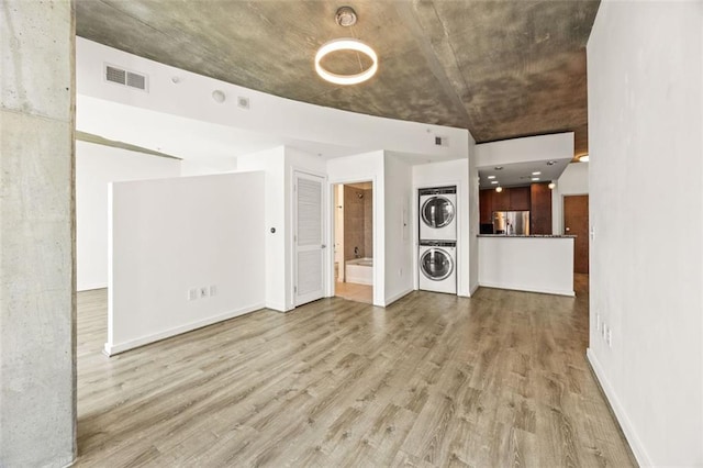 unfurnished living room with stacked washer / drying machine, wood finished floors, and baseboards