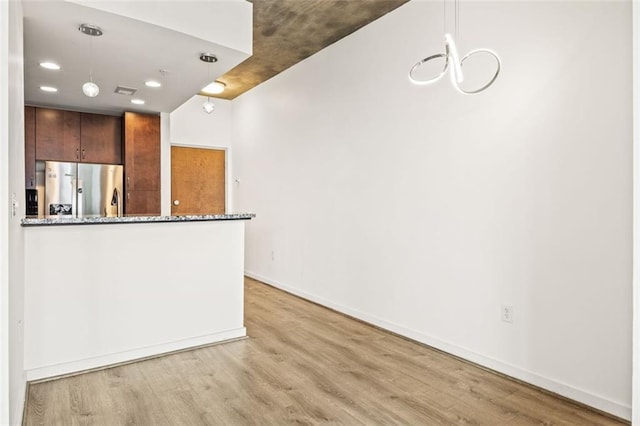 kitchen with stainless steel fridge, light wood-style flooring, dark stone countertops, a chandelier, and recessed lighting