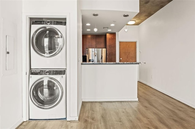 laundry area featuring stacked washing machine and dryer, light wood-style flooring, recessed lighting, baseboards, and electric panel