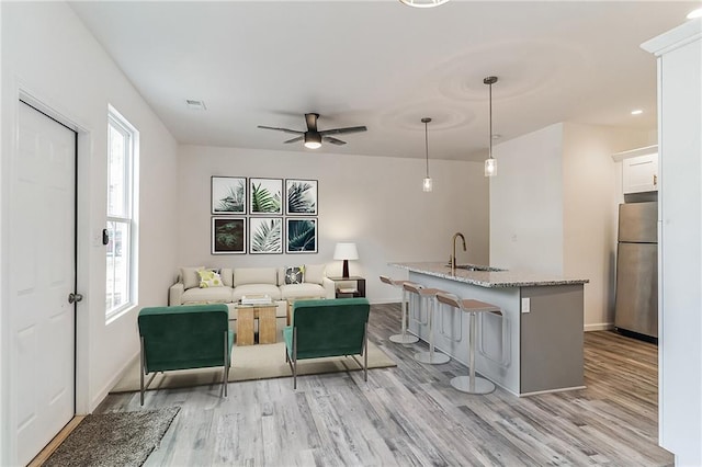 living room with visible vents, a ceiling fan, light wood-style flooring, and baseboards