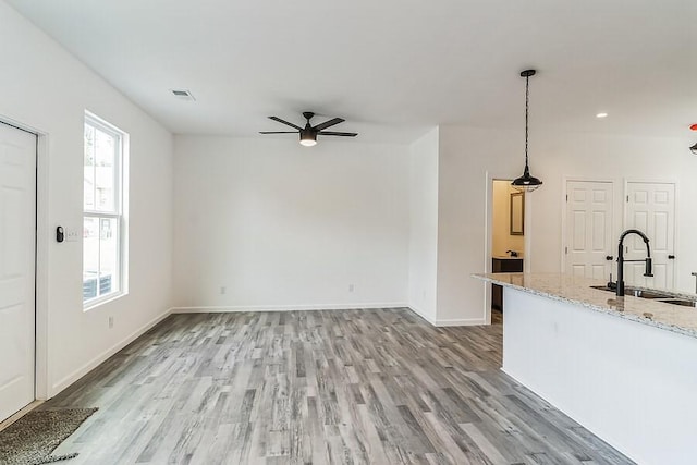 unfurnished living room featuring a sink, light wood finished floors, a ceiling fan, baseboards, and visible vents
