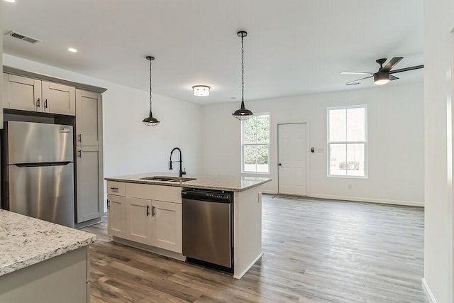 kitchen featuring ceiling fan, a sink, stainless steel appliances, wood finished floors, and a center island with sink
