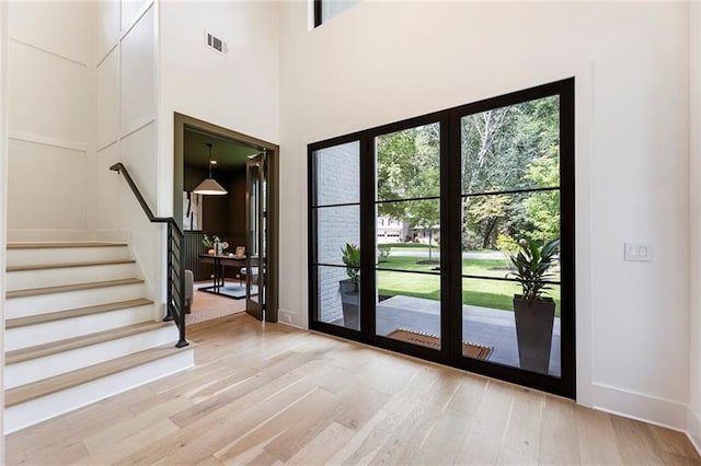 doorway to outside with light wood-type flooring and a towering ceiling