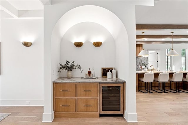 bar with light stone countertops, beverage cooler, decorative light fixtures, beamed ceiling, and light hardwood / wood-style floors