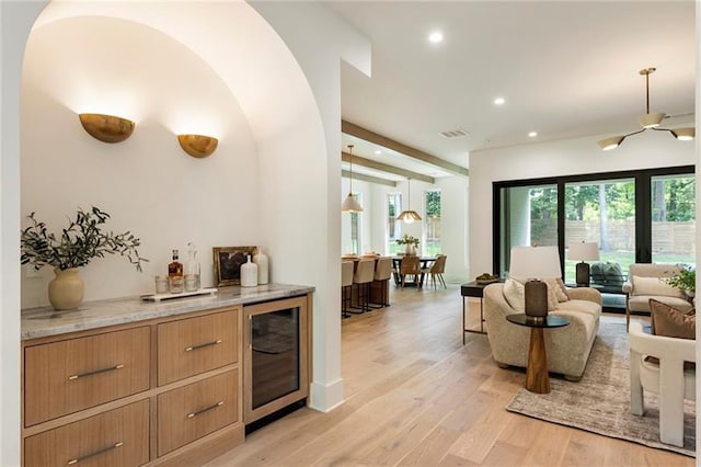 bar with beam ceiling, light stone countertops, wine cooler, pendant lighting, and light hardwood / wood-style floors