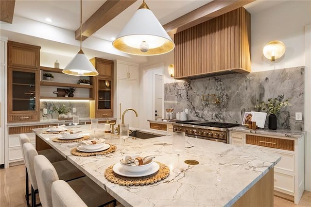 kitchen with backsplash, sink, hanging light fixtures, a large island, and light stone counters