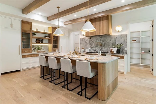 kitchen featuring beamed ceiling, pendant lighting, a center island with sink, and white cabinetry