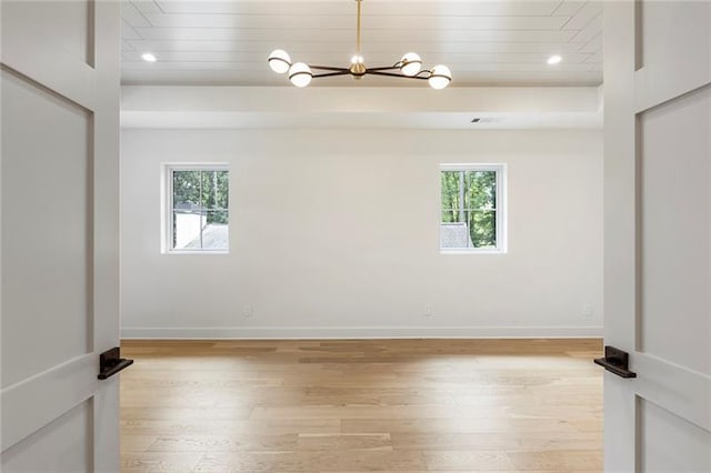 empty room featuring plenty of natural light, a chandelier, and light hardwood / wood-style flooring