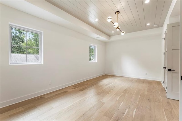 empty room with a raised ceiling, light wood-type flooring, and wooden ceiling