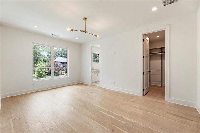 unfurnished bedroom with ensuite bath, a spacious closet, a notable chandelier, light hardwood / wood-style floors, and a closet