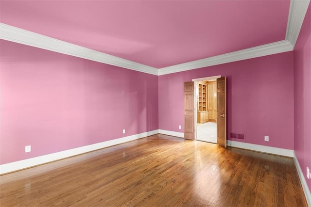 empty room with visible vents, crown molding, baseboards, and wood finished floors