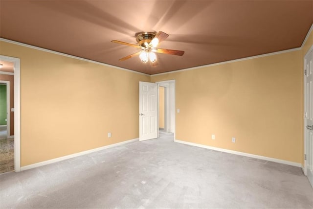 carpeted spare room with crown molding, baseboards, and ceiling fan