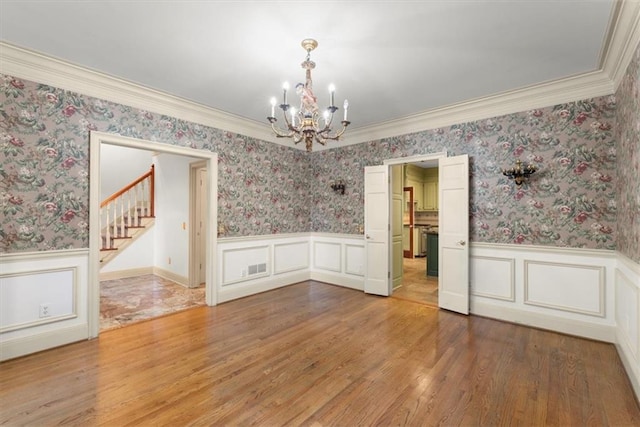 empty room with wallpapered walls, light wood-style floors, and a wainscoted wall