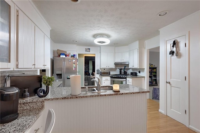 kitchen with appliances with stainless steel finishes, kitchen peninsula, light stone countertops, and light hardwood / wood-style floors