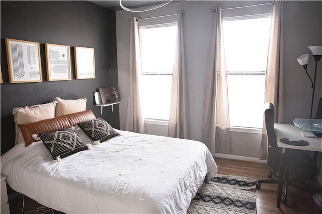 bedroom with multiple windows, baseboards, and wood finished floors