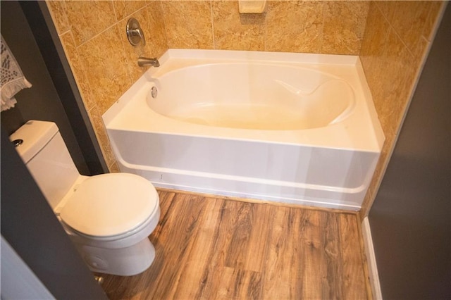 bathroom with a tub to relax in, toilet, and wood finished floors