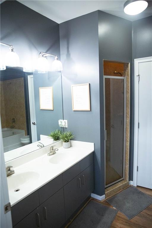 full bath featuring double vanity, wood finished floors, a stall shower, and a sink