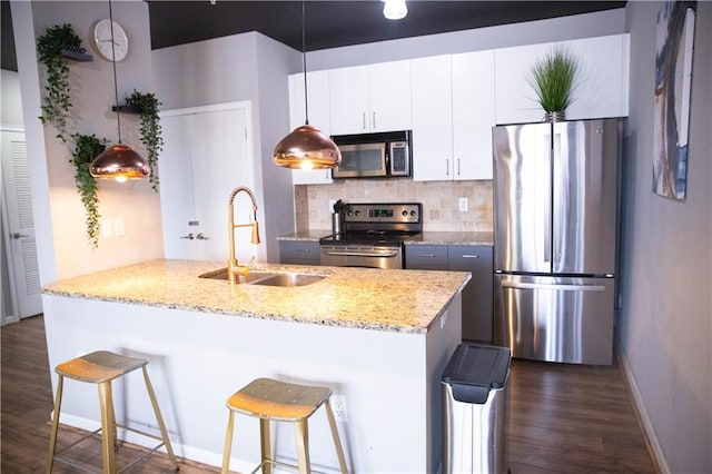 kitchen with pendant lighting, appliances with stainless steel finishes, white cabinetry, a sink, and a kitchen breakfast bar