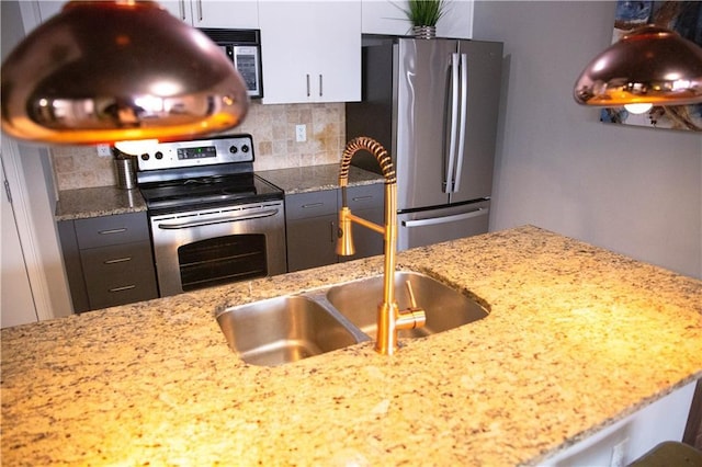 kitchen with stainless steel appliances, decorative backsplash, white cabinetry, a sink, and light stone countertops