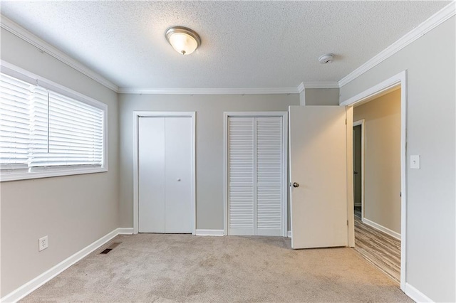 unfurnished bedroom with baseboards, visible vents, ornamental molding, multiple closets, and carpet flooring