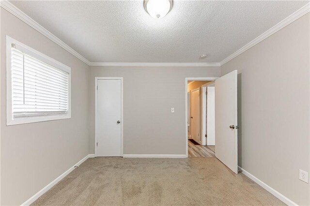 unfurnished bedroom with baseboards, light colored carpet, ornamental molding, and a textured ceiling