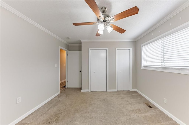 unfurnished bedroom with crown molding, baseboards, two closets, and light carpet