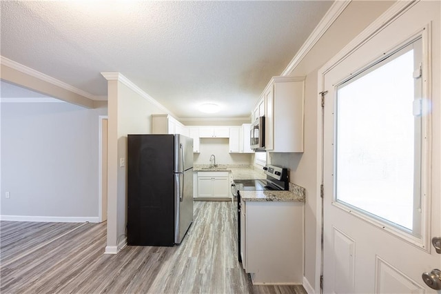 kitchen featuring baseboards, a sink, ornamental molding, appliances with stainless steel finishes, and light wood-type flooring