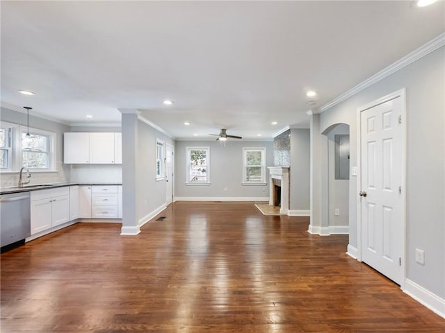 unfurnished living room with crown molding, a fireplace, dark wood finished floors, a ceiling fan, and baseboards