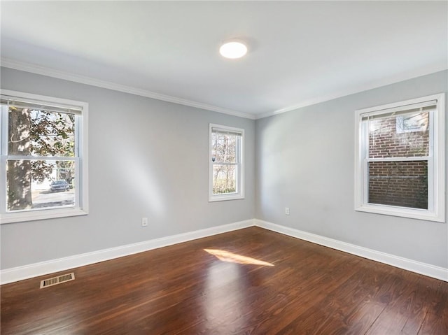 spare room with dark wood-style floors, visible vents, crown molding, and baseboards