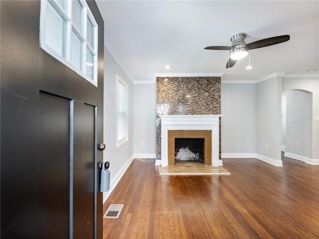 unfurnished living room with crown molding, visible vents, a fireplace with raised hearth, and wood finished floors