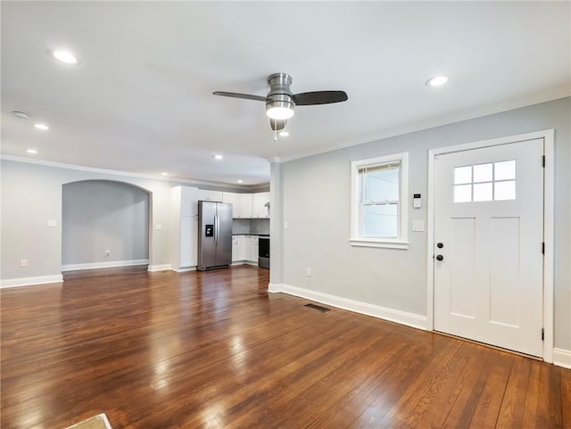 unfurnished living room with ornamental molding, dark wood-type flooring, arched walkways, and baseboards