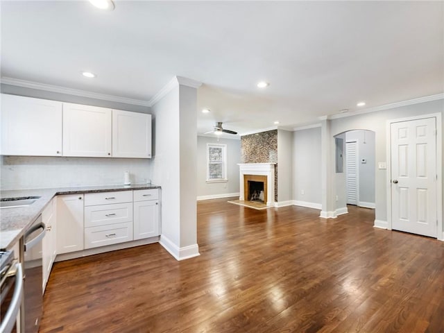 kitchen with arched walkways, a large fireplace, light stone counters, and white cabinetry