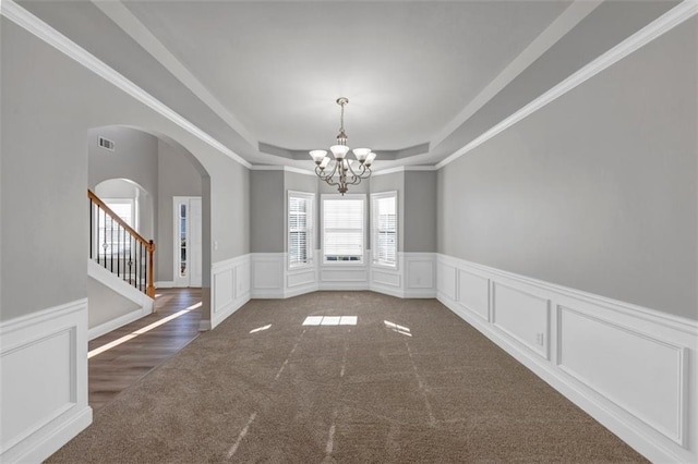 carpeted empty room with a tray ceiling, ornamental molding, and a notable chandelier